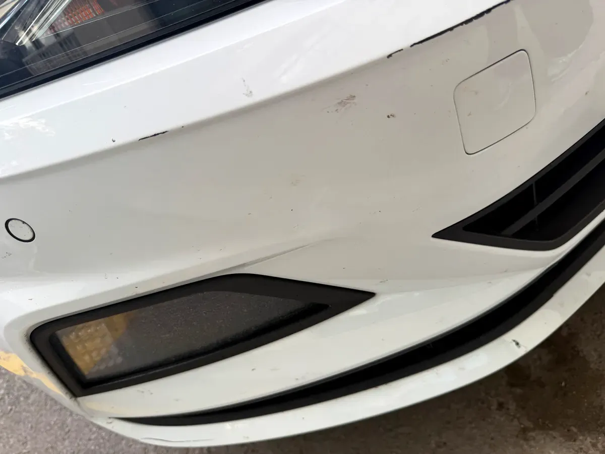 Beyaz aracın ön tamponunda yüzeysel çizikler ve far detayı, pasta cila öncesi